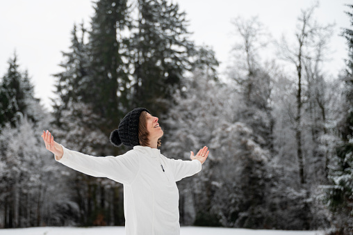 Happy peaceful young woman standing outside in a snowy winter nature enjoying life with her arms spread widely.