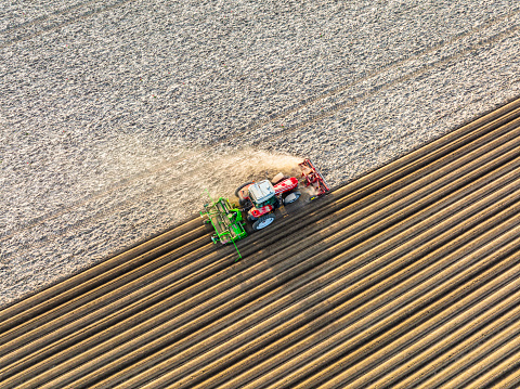 Tractorplanting seed potatoes in prepared soil for planting crops during a sunny and dry springtime day. Aerial view drone view from directly above.