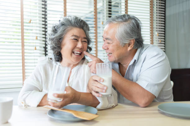 nonno e nonna cinesi che giocano e tengono insieme bicchieri di latte - 60s senior adult breakfast cheerful foto e immagini stock