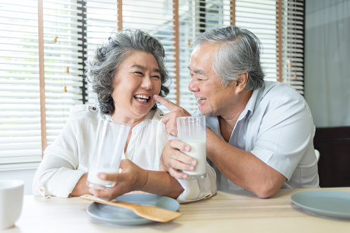 Chinese Grandfather and Grandmother playing and holding glasses of milk together at home, Drinking