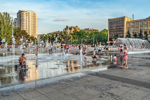 Mykolaiv, Ukraine - July 25, 2020: People have fun in the city square with pedestrian and arched fountains on a summer evening in Mykolaiv. Happy pastime of citizens and tourists