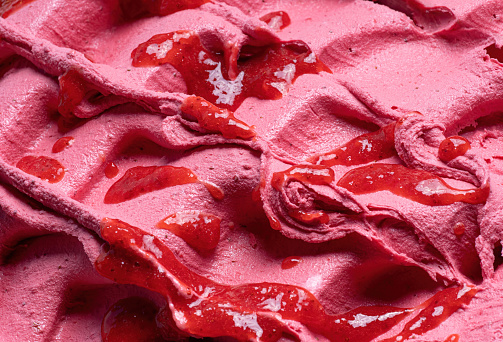 Frozen Strawberry flavour gelato - full frame detail. Close up of a pink surface texture of Ice cream covered with pieces of red fruit.