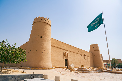 Al Masmak Fort and Palace exterior view with Saudi Arabian national flag on sunny day