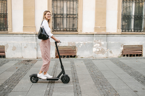 A young beautiful businesswoman with business bag riding electric scooter