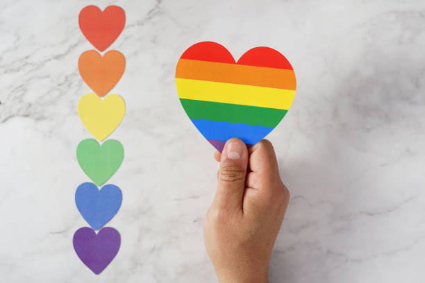 mano de un hombre sosteniendo un corazón con los colores lgbtq junto a varios corazones pequeños con los mismos colores del movimiento sobre un fondo de mármol. concepto de tolerancia, diversidad e inclusión. - lesbian gay man rainbow multi colored fotografías e imágenes de stock