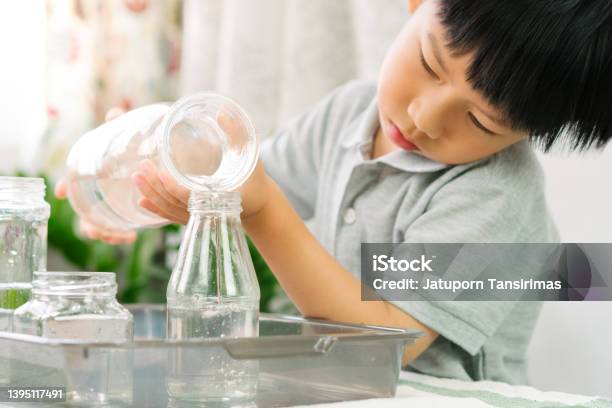 Cute Asian Little Montessori Boy Pouring Water Into Glass Water Bottles Stock Photo - Download Image Now