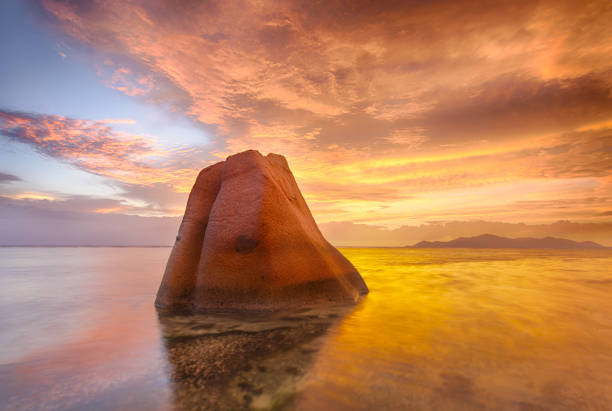 Lonely rock reflecting in the sea during beautiful vibrant sunset. Island of La Digue, Seychelles
