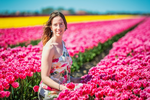 dutch woman seated looking the pink tulip flowers in the spring in the Netherlands smiling and looking at camera