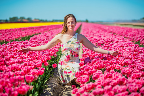 dutch woman crouched and surrounded by pink tulip flowers in the spring in the Netherlands smiling and looking at camera