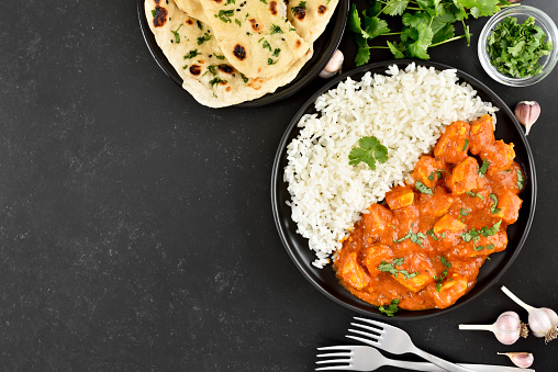 Indian chicken curry with rice on plate over dark stone background. Top view, flat lay