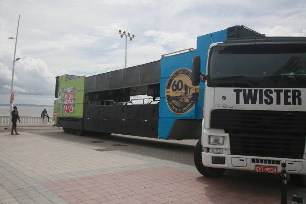 A blue toy truck is sitting on a road. The truck is small and has a red stripe on it. The road is empty and the sky is cloudy