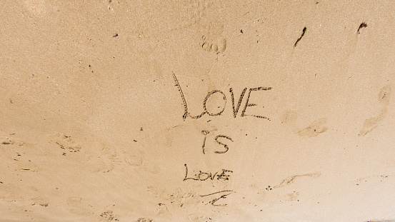 On the sand of the beach someone has written a message of love is love, nobody can be seen, with copy space