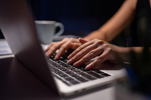 Close-up of young woman's hands working on laptop at night at home