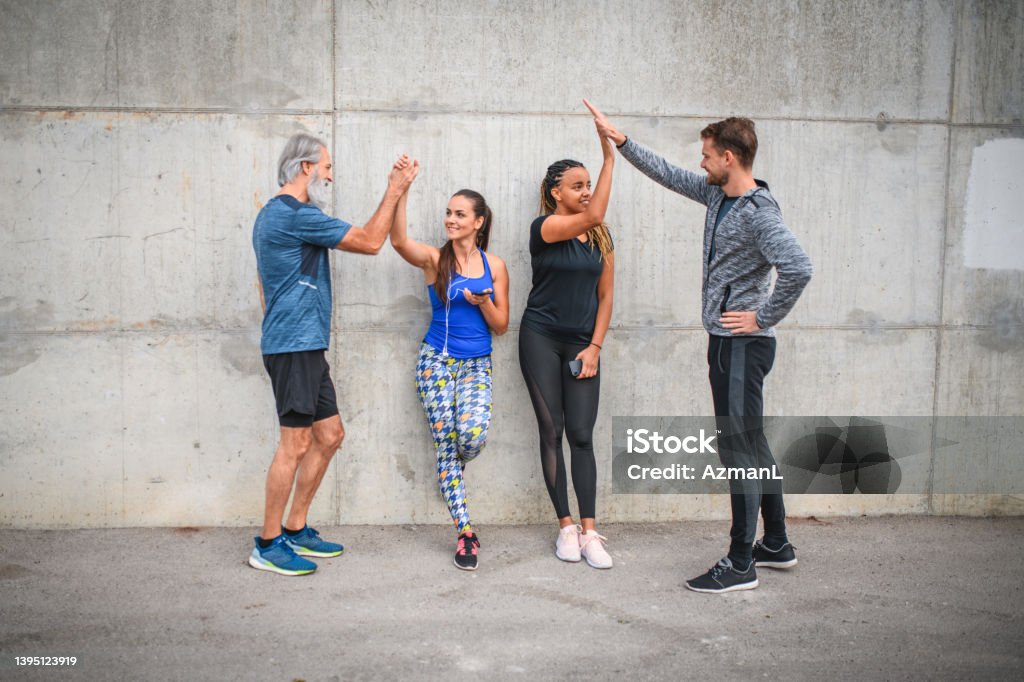 Athletic Group Of Friends Motivating And Supporting Each Other Full length front view of athletic group of friends motivating and supporting each other after exercising. They are wearing sports clothing and doing high five. Running Stock Photo