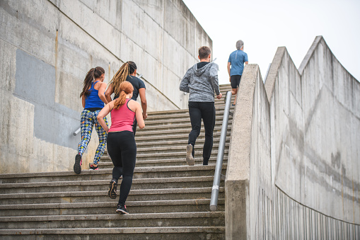 Low angle view of athletes training outdoors on concrete stairs. They are building strength and endurance with hiit and cardio exercises. They are wearing activewear.