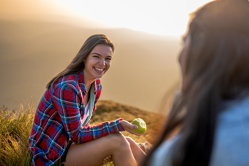 Portrait of young woman sitting and smiling on top of mountain.