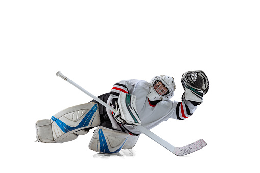 Portrait of teen boy, hockey player, goalkeeper catching plug in motion isolated over white studio background. Dynamic sport. Concept of sportive lifestyle, childhood, hobby, action