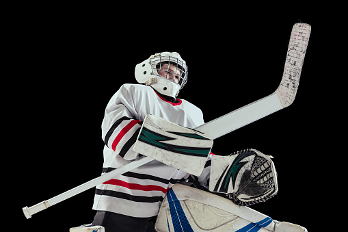Portrait of teen boy, hockey player, goalkeeper training isolated over black studio background. Dynamic sport. Concept of sportive lifestyle, childhood, hobby, action. Copy space for ad