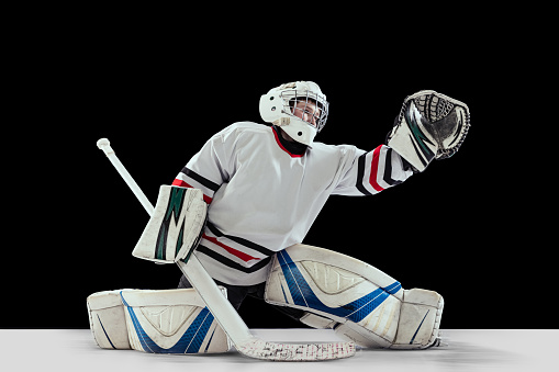 Dynamic portrait of teen boy, hockey player, goalkeeper catching puck with special glove isolated on black studio background. Concept of sportive lifestyle, childhood, hobby, action. Copy space for ad