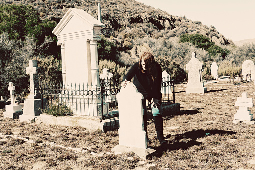 A woman dressed in black looks at old tomb stones in a cemetery
