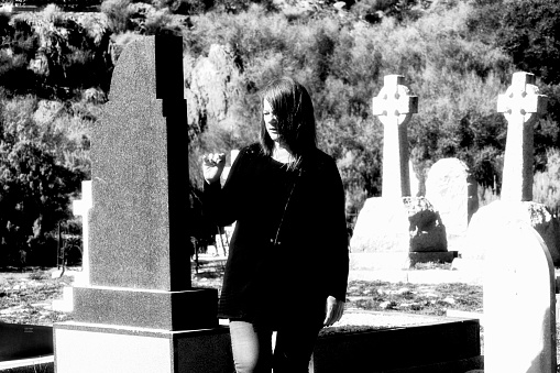A woman dressed in black looks at old tomb stones in a cemetery
