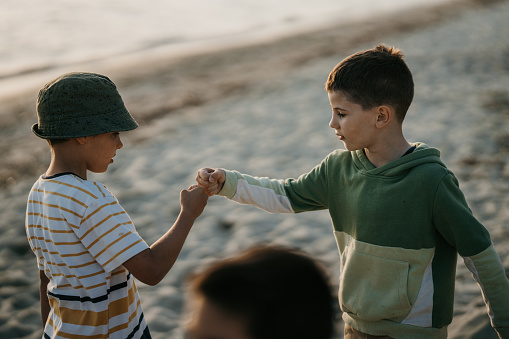 Two cheerful boys, friends or siblings, playing rock paper scissors hand game on sandy beach