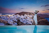 A stands by the swimming pool and enjoys the sunset view over the illuminated village of Oia