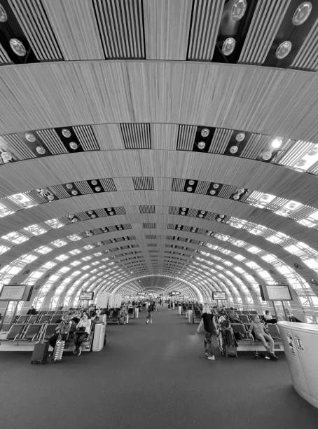 Perspective view of Paris-Charles de Gaulle (Roissy, CDG) - Terminal 2E - Gates K boarding halls in black and white. Passengers are seated looking outside the windows waiting for their flights to board. Photo taken in CDG on May 2nd, 2022.