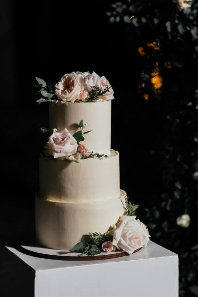 istock Wedding cake. Cake three tiers on a beige table, decorated with roses on a dark background 1395132995