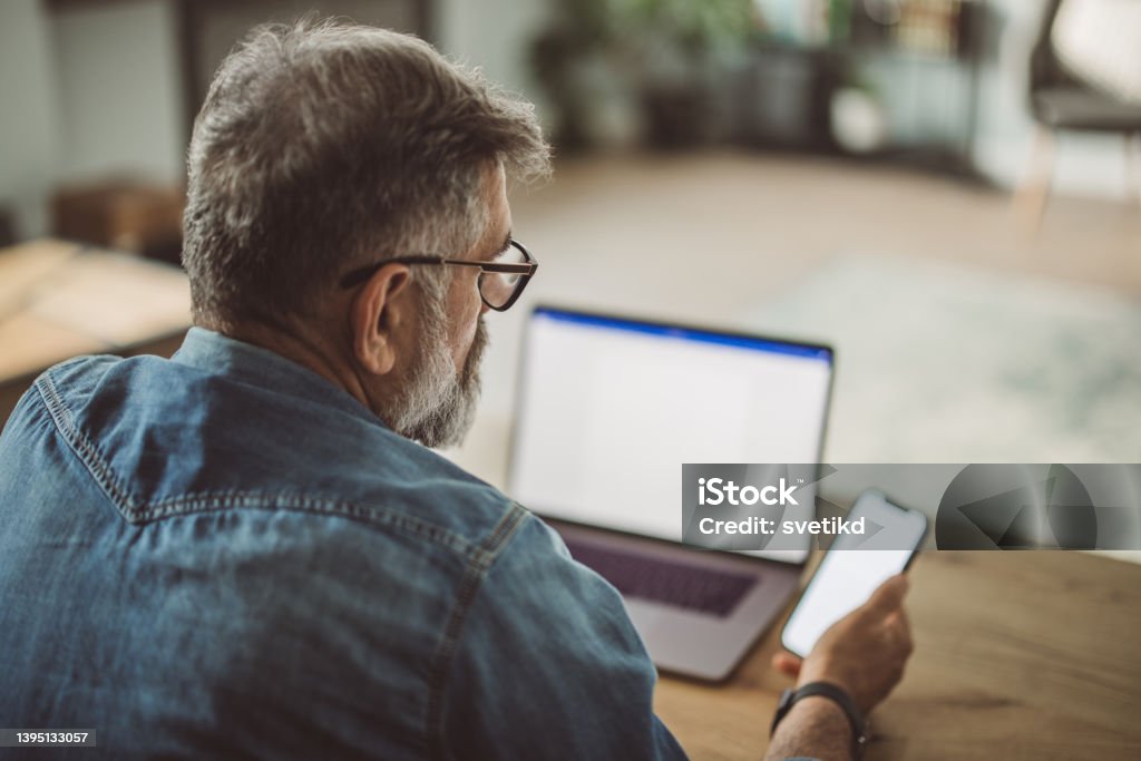 Mature man working from home office Mature man sitting at the table and working on laptop. Computer Monitor Stock Photo