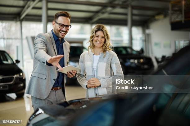 Happy Salesman Selling The Car To His Female Customer In A Showroom Stock Photo - Download Image Now