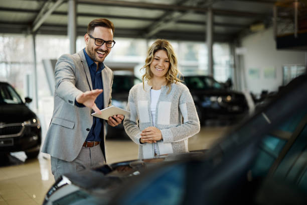 happy salesman selling the car to his female customer in a showroom. - professional dealer imagens e fotografias de stock