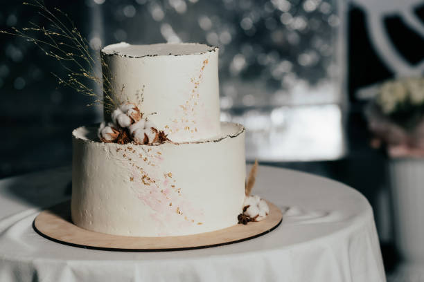 istock A wedding cake. Milk-colored cake decorated with cotton beads and gold leaf on a dark background in wedding day 1395134738