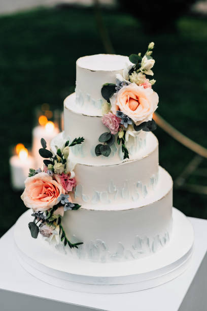 istock A wedding cake. Appetizing white cake four tiers on a beige table, decorated with roses, eucalyptus, on a light green background 1395134790
