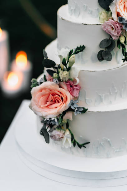 istock A wedding cake. Appetizing white cake four tiers on a beige table, decorated with roses, eucalyptus, on a light green background close-up 1395134797