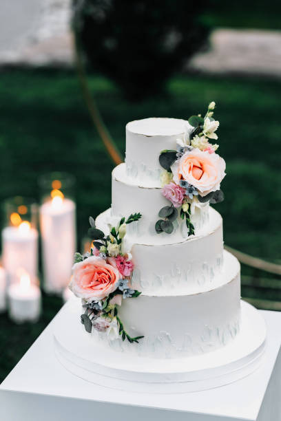 istock A wedding cake. Appetizing white cake four tiers on a beige table, decorated with roses, eucalyptus, on a light green background 1395134804