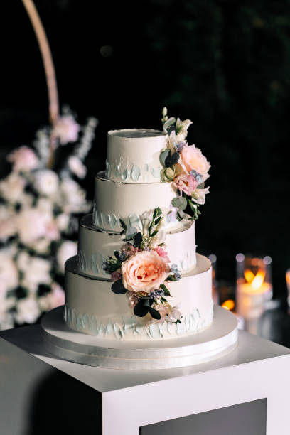 istock A wedding cake. Appetizing white cake four tiers on a beige table, decorated with roses, eucalyptus, on a black green background 1395134845