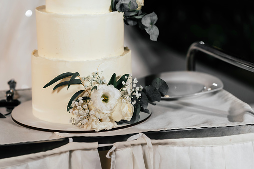 A wedding cake. Appetizing cake three tiers on a beige table, decorated roses, eucalyptus, gold leaf on a dark background
