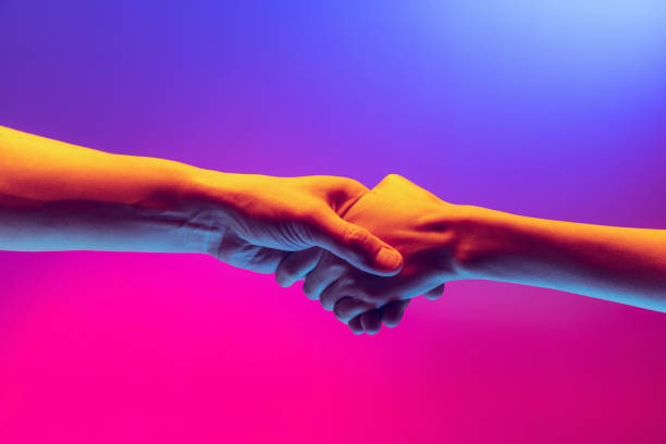 Handshake. Male and female hands touching each other on gradient blue and pink background in neon. Concept of human rights, social issues, gathering. stock photo