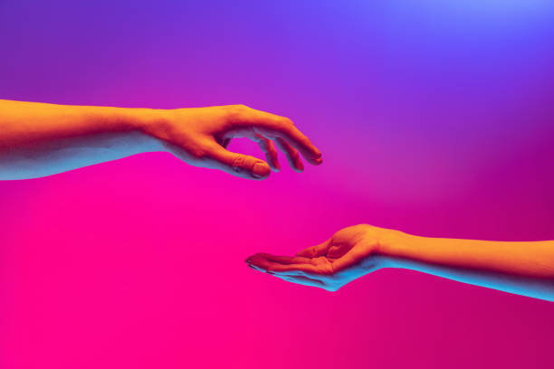 istock Two authentic hands trying to touch each other isolated on gradient background in neon light. Concept of relationship, community, care, support, symbolism, culture 1395134850