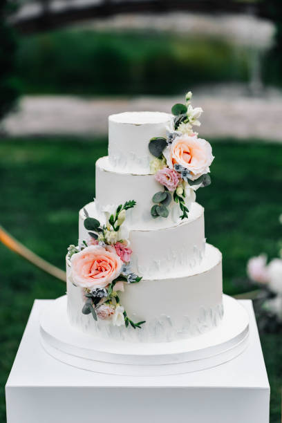 istock A wedding cake. Appetizing white cake four tiers on a beige table, decorated with roses, eucalyptus, on a light green background 1395134956