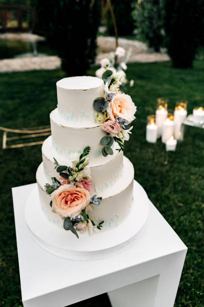 istock A wedding cake. Appetizing white cake four tiers on a beige table, decorated with roses, eucalyptus, on a light green background 1395135019