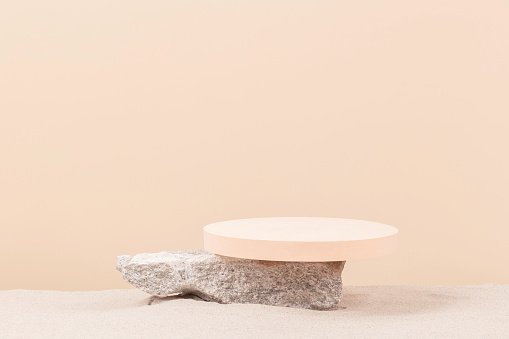 Grunge concrete stone and beige round platform podium for cosmetics or products on white beach sand background. Front view.