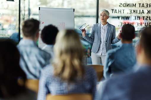 Mature female CEO giving a presentation to group of her colleagues in board room.