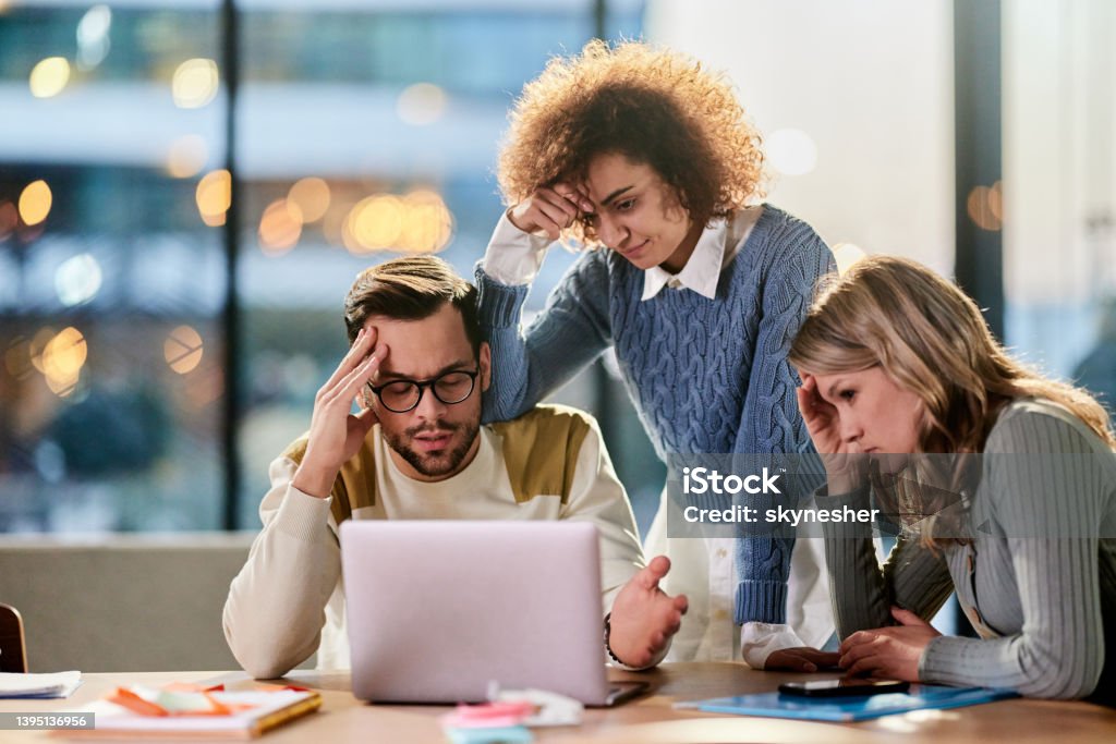 Worried creative team working on laptop in the office. Group of entrepreneurs feeling displeased while reading problematic e-mail on a computer in the office. Problems Stock Photo