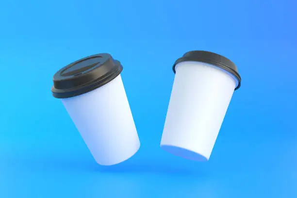 Photo of Two disposable paper coffee cup with black lid in the air over blue background