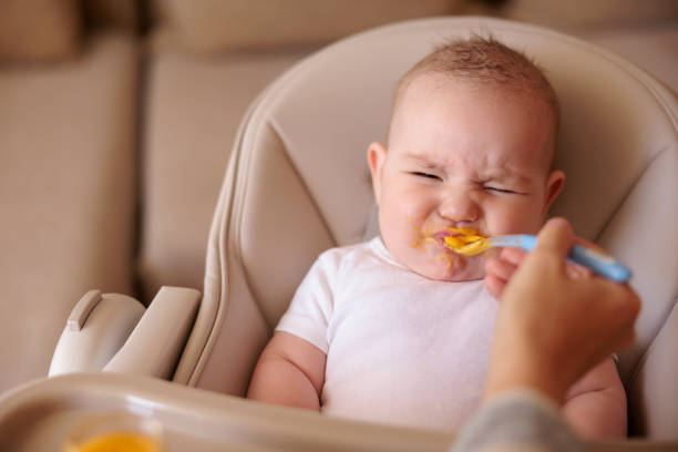 Baby making funny faces while refusing to eat porridge stock photo