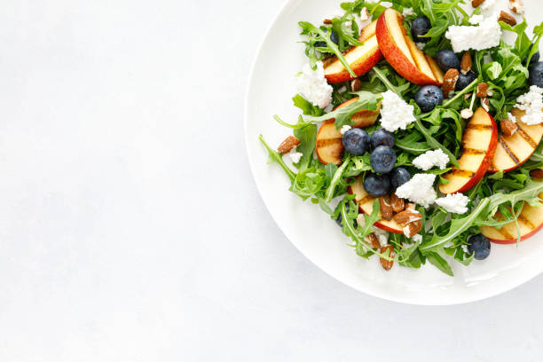 istock Peach, blueberry and arugula fresh fruit salad with cheese and almond nuts, top view 1395140913