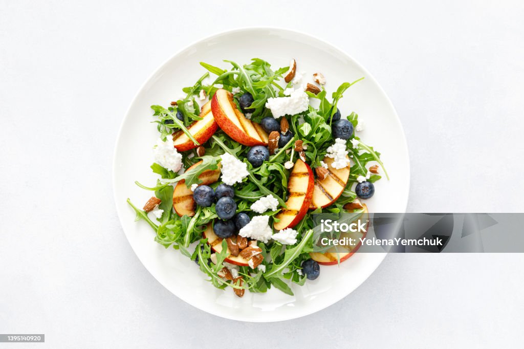 Peach, blueberry and arugula fresh fruit salad with cheese and almond nuts, top view Salad Stock Photo