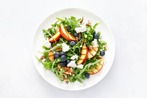 салат из свежих фруктов из персика, черники и рукколы с сыром и миндальными орехами, вид сверху - antioxidant blueberry fruit berry fruit стоковые фото и изображения